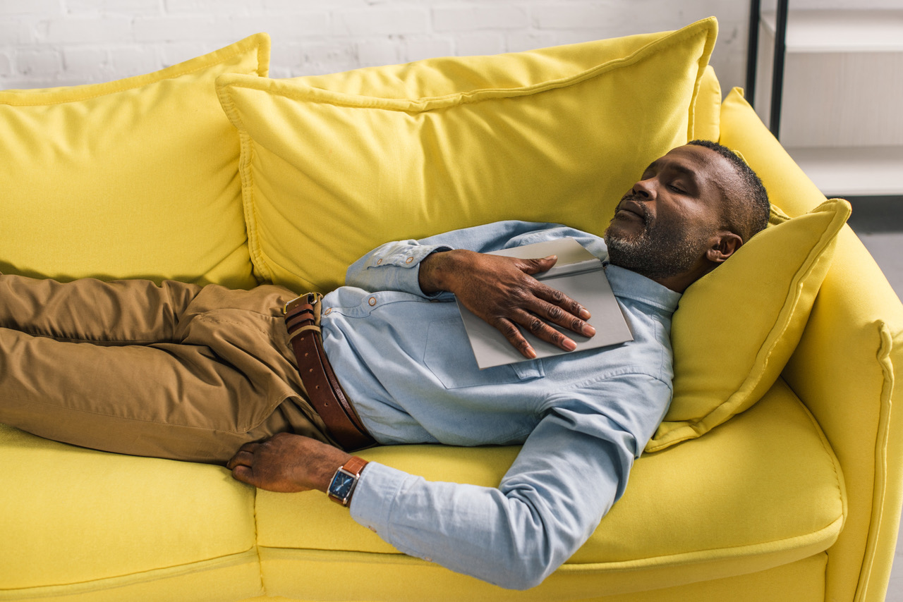 high angle view of senior african american man sleeping with book on sofa